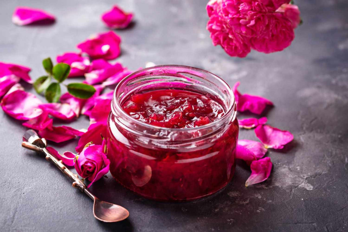 A jar of pink rose jam filled with delicate rose petals on top, showcasing its floral flavor and vibrant color.