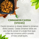 Cinnamon Cassia Sticks product info card on a light grey stone-textured background with a black square bowl of golden-brown broken cassia bark chips and a large whole rolled cassia bark piece at the top left, fresh green cassia leaves scattered around, describing cassia sticks as single thick-layered hard bark unlike multi-layered real Ceylon cinnamon.
