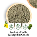 Top-down view of a round light wooden bowl filled with coarse grey-green Gokshura Tribulus terrestris powder on a white background, flanked by a fresh yellow A Gokshura flower with feathery leaves at the bottom left and a spiky raw Gokshura fruit at the bottom right, displaying three green circular badges for Vegan, 100% Organic, and Gluten-Free certifications, captioned "Product of India". "Packaged in Canada."