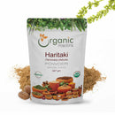 Organic Mantra Haritaki (Terminalia chebula) Powder, 227g standup pouch with USDA Organic and OneCert certifications, origin India, surrounded by whole dried Haritaki fruits, loose powder, and flowering plant sprigs.