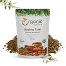 Organic Mantra Krishna Tulsi Ocimum tenuiflorum Holy Basil Powder 227g pouch with USDA Organic and OneCert certifications, origin India, surrounded by a mound of brown tulsi powder and fresh purple tulsi sprigs.