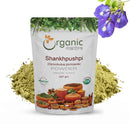 Organic Mantra Shankhpushpi (Convolvulus pluricaulis) A 227g standup pouch of powder with USDA Organic and OneCert certifications, origin India, is displayed over a mound of olive-green powder with blue-purple shankhpushpi flowers in the corner.