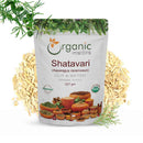 Organic Mantra Shatavari Asparagus racemosus Cut and Sifted 227g white resealable standing pouch with USDA Organic and OneCert Organic certifications and India origin label, centered on a white background surrounded by a large mound of pale cream cut root pieces, a fresh Asparagus racemosus fern branch with green berries at the top left, and a delicate red-berried shatavari sprig at the bottom right.