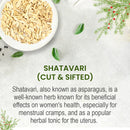 Shatavari cut and sifted product info card on a light grey stone-textured background with a white bowl of pale root pieces at the top left, scattered small green leaves and black pepper seeds, and decorative green Asparagus racemosus fern sprigs with red berries in the corners, describing Shatavari as an Ayurvedic herb beneficial for women's menstrual health and as a uterine tonic.