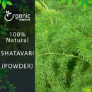 Organic Mantra 100% Natural Shatavari Powder product banner with a brand logo on a dark leafy left panel beside a vivid outdoor close-up photograph of a dense Asparagus racemosus plant with lush, feathery, needle-like, bright green foliage spreading across the entire frame.