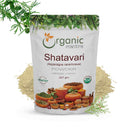 Organic Mantra Shatavari Asparagus racemosus Powder 227g white resealable standing pouch with USDA Organic and OneCert Organic certifications and India origin label, centered on a white background with a pale beige powder splash behind it, a fresh Asparagus racemosus fern branch with green berries at the top left, and a delicate red-berried shatavari sprig at the bottom right.