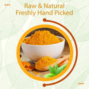 Turmeric powder in a white bowl with a wooden spoon, fresh turmeric root slices, and green leaves, labeled Raw and Natural, Freshly Hand Picked.
